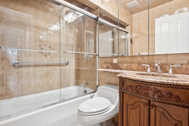 full bathroom featuring toilet, tile walls, combined bath / shower with glass door, and vanity