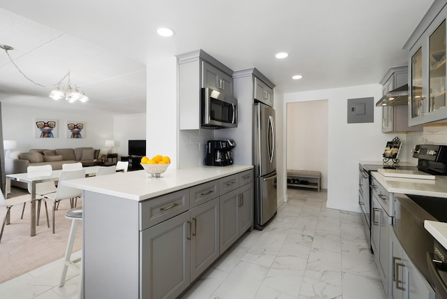 kitchen featuring a kitchen bar, appliances with stainless steel finishes, electric panel, gray cabinets, and backsplash