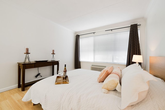 bedroom with crown molding, a wall unit AC, and light hardwood / wood-style floors