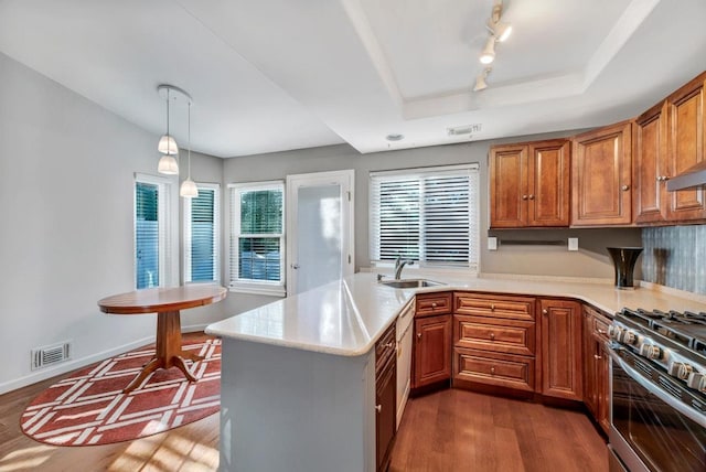 kitchen with stainless steel stove, hanging light fixtures, kitchen peninsula, dark hardwood / wood-style flooring, and a raised ceiling