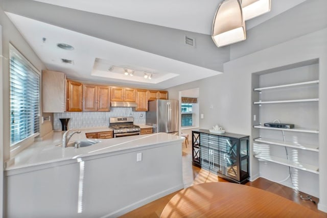 kitchen with appliances with stainless steel finishes, sink, kitchen peninsula, a raised ceiling, and light hardwood / wood-style flooring