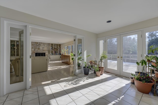 sunroom / solarium with plenty of natural light, a stone fireplace, and french doors