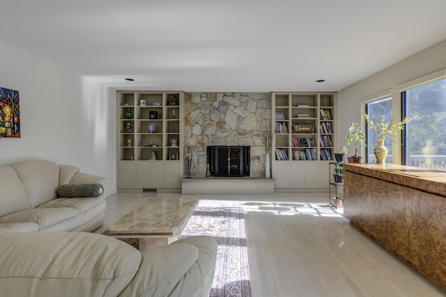 living room with a stone fireplace, built in features, and light hardwood / wood-style flooring