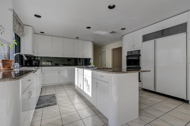 kitchen with sink, white cabinets, decorative backsplash, built in refrigerator, and a center island