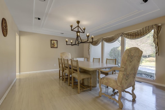 dining area featuring a notable chandelier, a tray ceiling, light wood-style flooring, and baseboards