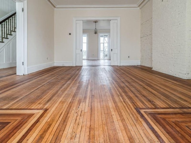 unfurnished living room featuring crown molding, brick wall, and hardwood / wood-style floors