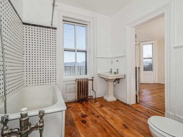 bathroom with sink, radiator, hardwood / wood-style flooring, a bathing tub, and toilet