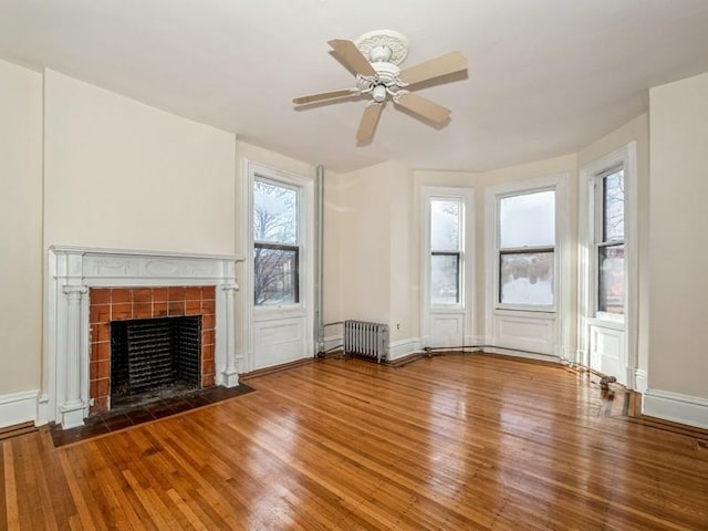 unfurnished living room featuring radiator heating unit, a fireplace, wood-type flooring, and ceiling fan