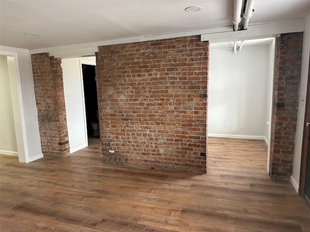 spare room featuring brick wall and dark wood-type flooring