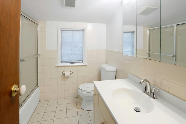 full bathroom featuring bath / shower combo with glass door, tile walls, vanity, toilet, and tile patterned floors