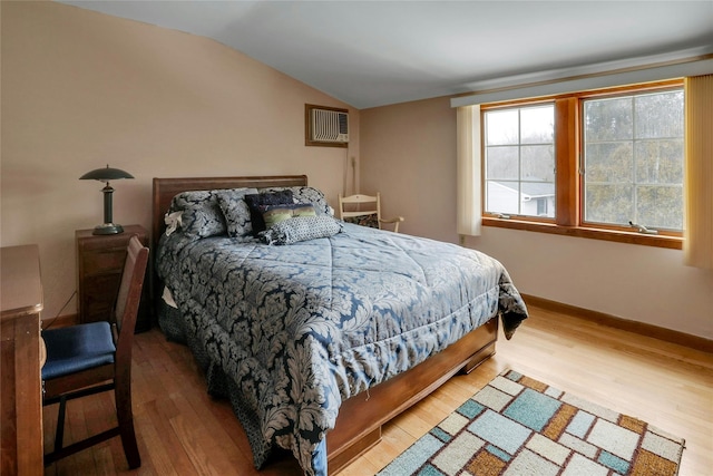 bedroom with vaulted ceiling, hardwood / wood-style floors, and an AC wall unit