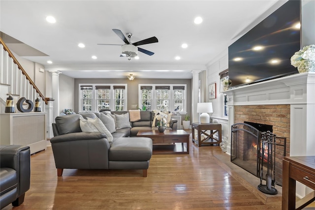 living room featuring a brick fireplace, hardwood / wood-style flooring, ceiling fan, and ornate columns