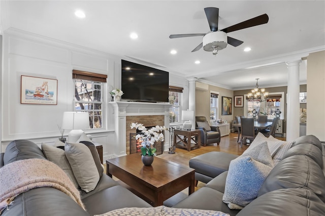 living room with crown molding, ceiling fan with notable chandelier, decorative columns, and hardwood / wood-style floors