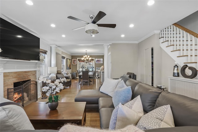 living room with a brick fireplace, crown molding, wood-type flooring, and decorative columns