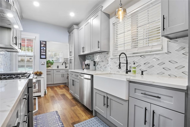 kitchen featuring sink, light hardwood / wood-style flooring, gray cabinets, stainless steel appliances, and decorative light fixtures