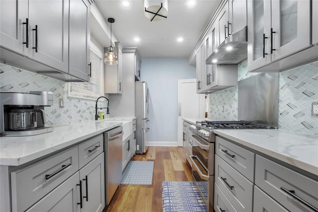 kitchen featuring wall chimney range hood, decorative light fixtures, gray cabinets, and stainless steel appliances