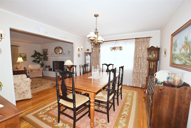 dining room with a fireplace, ornamental molding, a chandelier, and light wood-type flooring