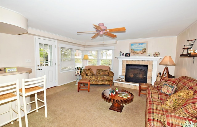 living room with a tile fireplace, crown molding, light colored carpet, and ceiling fan