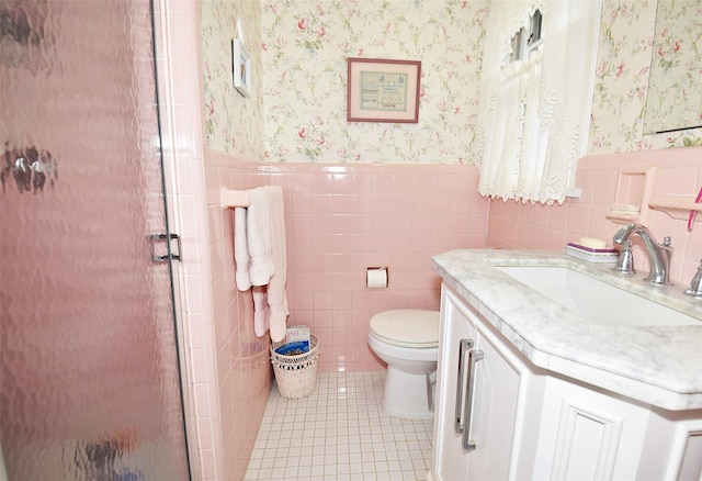 bathroom featuring toilet, a shower with shower door, tile walls, vanity, and tile patterned flooring