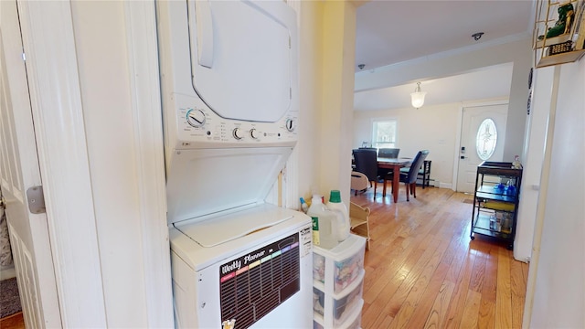 laundry area featuring crown molding, stacked washer and clothes dryer, and light wood-type flooring