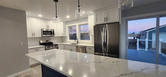 kitchen with light stone counters, hanging light fixtures, white cabinets, stainless steel appliances, and backsplash