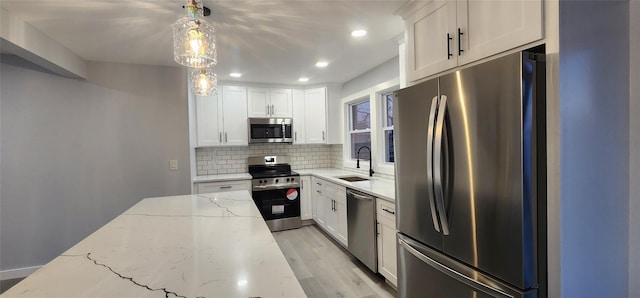 kitchen with sink, pendant lighting, stainless steel appliances, light stone countertops, and white cabinets