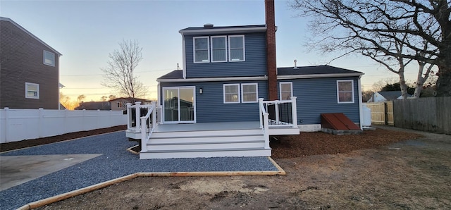 back house at dusk with a wooden deck and a patio