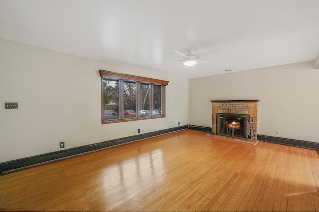 unfurnished living room featuring hardwood / wood-style floors, a stone fireplace, and ceiling fan