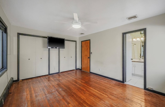 unfurnished bedroom with ensuite bath, light wood-type flooring, multiple closets, a baseboard radiator, and ceiling fan