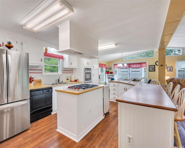 kitchen featuring wood-type flooring, a center island, vaulted ceiling, appliances with stainless steel finishes, and white cabinets