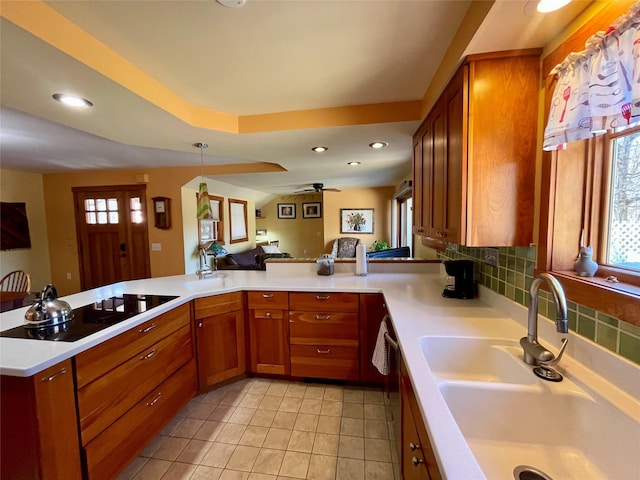 kitchen featuring tasteful backsplash, sink, hanging light fixtures, black electric stovetop, and kitchen peninsula