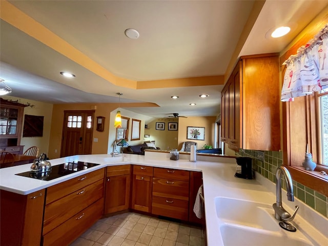 kitchen featuring sink, hanging light fixtures, backsplash, black electric cooktop, and kitchen peninsula