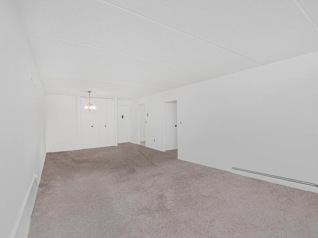 carpeted spare room featuring a chandelier and baseboard heating