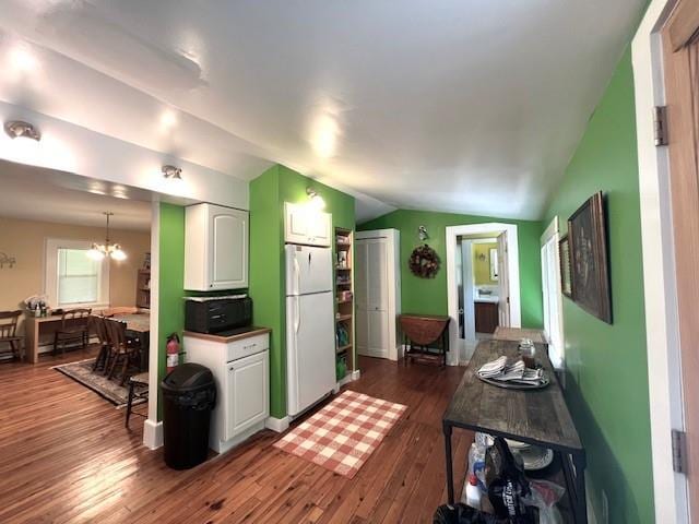 kitchen featuring dark wood-type flooring, white cabinetry, a notable chandelier, vaulted ceiling, and white fridge