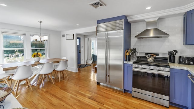 kitchen with wall chimney range hood, blue cabinetry, light hardwood / wood-style floors, and appliances with stainless steel finishes