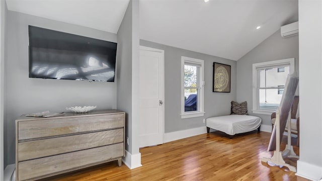 sitting room with vaulted ceiling, an AC wall unit, and wood-type flooring