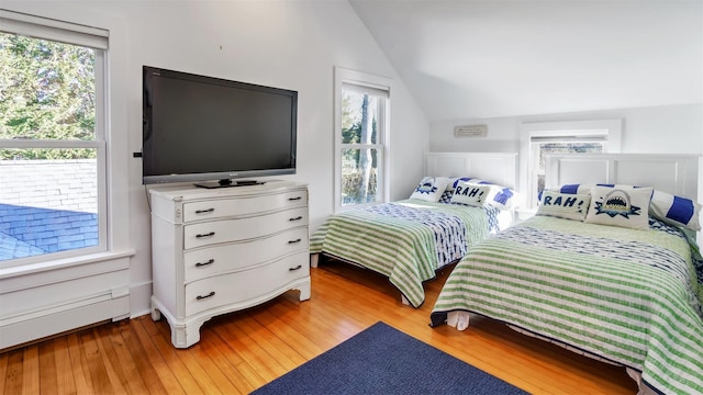 bedroom with light hardwood / wood-style floors, vaulted ceiling, and a baseboard heating unit