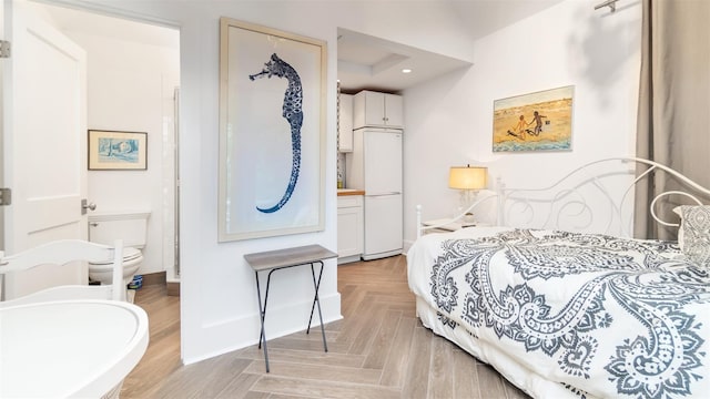 bedroom with light parquet floors, white fridge, and ensuite bath