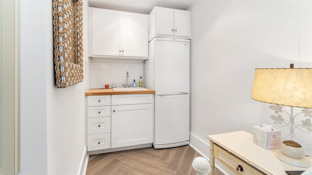 kitchen featuring butcher block counters, sink, white cabinets, white refrigerator, and light parquet floors