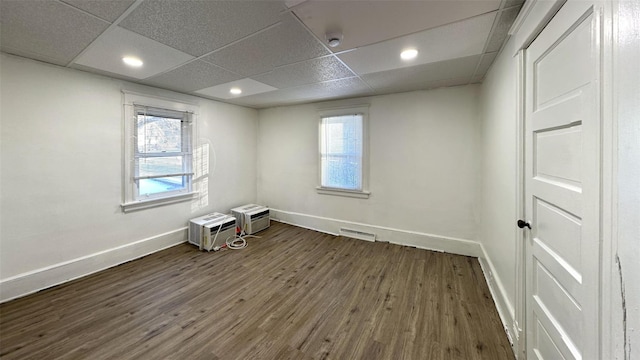 unfurnished room with an AC wall unit, a healthy amount of sunlight, a paneled ceiling, and dark hardwood / wood-style flooring