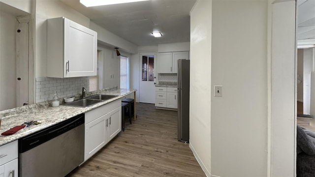 kitchen featuring sink, appliances with stainless steel finishes, white cabinetry, light hardwood / wood-style floors, and decorative backsplash