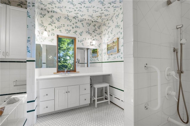 bathroom with tile walls, tile patterned flooring, a baseboard heating unit, tiled shower, and vanity