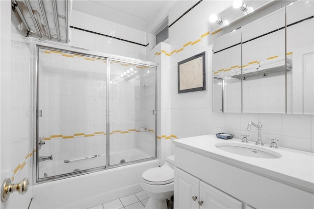 full bathroom with bath / shower combo with glass door, tile walls, tile patterned flooring, vanity, and toilet