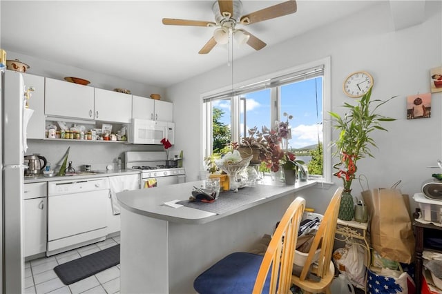 kitchen featuring a breakfast bar, light tile patterned floors, kitchen peninsula, white appliances, and white cabinets