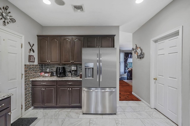 kitchen featuring light stone countertops, stainless steel fridge, dark brown cabinetry, and decorative backsplash