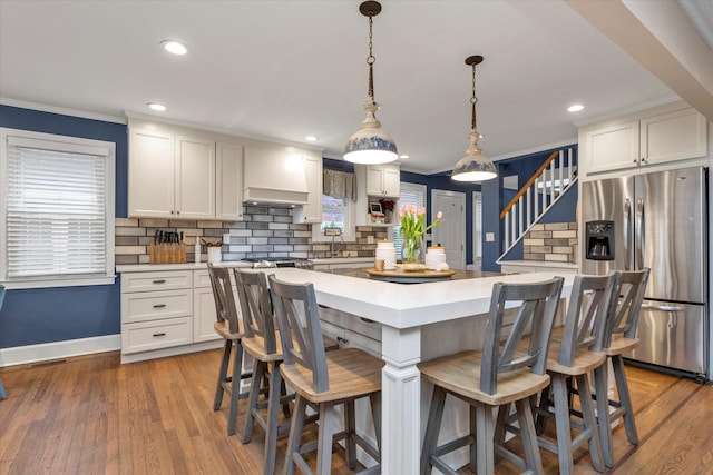 kitchen with white cabinetry, decorative backsplash, hanging light fixtures, a center island, and stainless steel fridge with ice dispenser