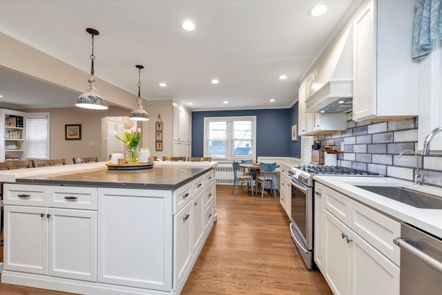 kitchen featuring stainless steel appliances, decorative light fixtures, custom range hood, and white cabinets