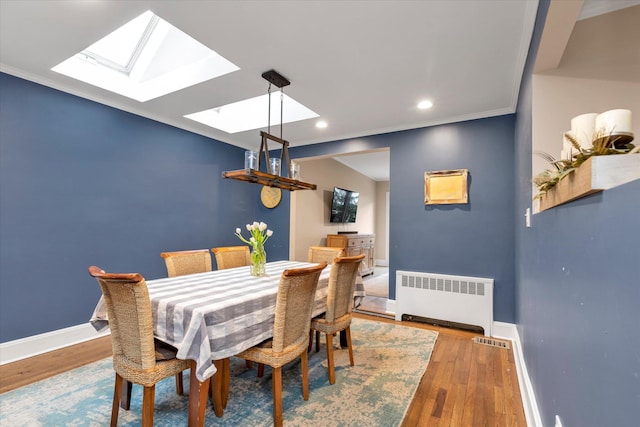 dining area featuring hardwood / wood-style floors, crown molding, radiator heating unit, and a skylight