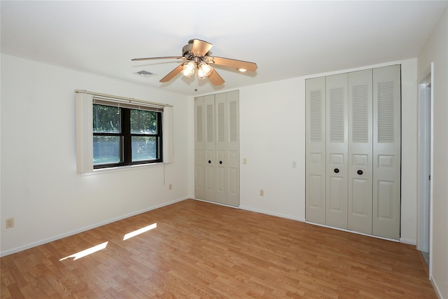 unfurnished bedroom featuring ceiling fan, light wood-type flooring, and two closets