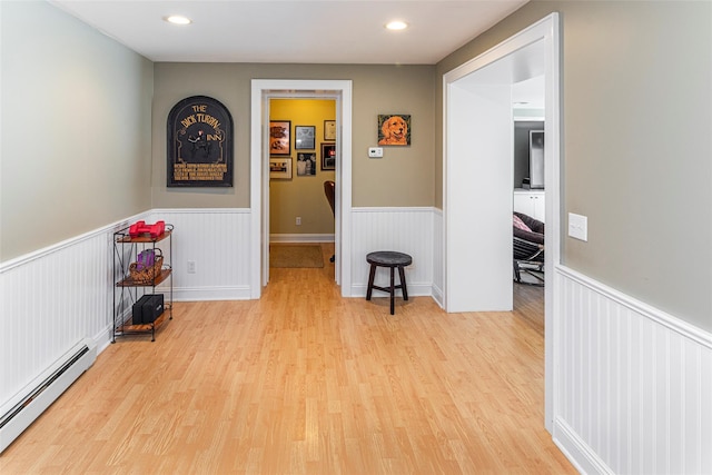 hall featuring a baseboard radiator, a wainscoted wall, and light wood finished floors